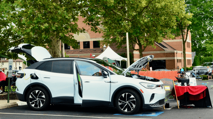 A white VW ID4 is parked in a disability parking spot with its trunk, front side doors, and frunk popped open as event attendees check out the electric vehicles. Shared by Drive Electric Dayton